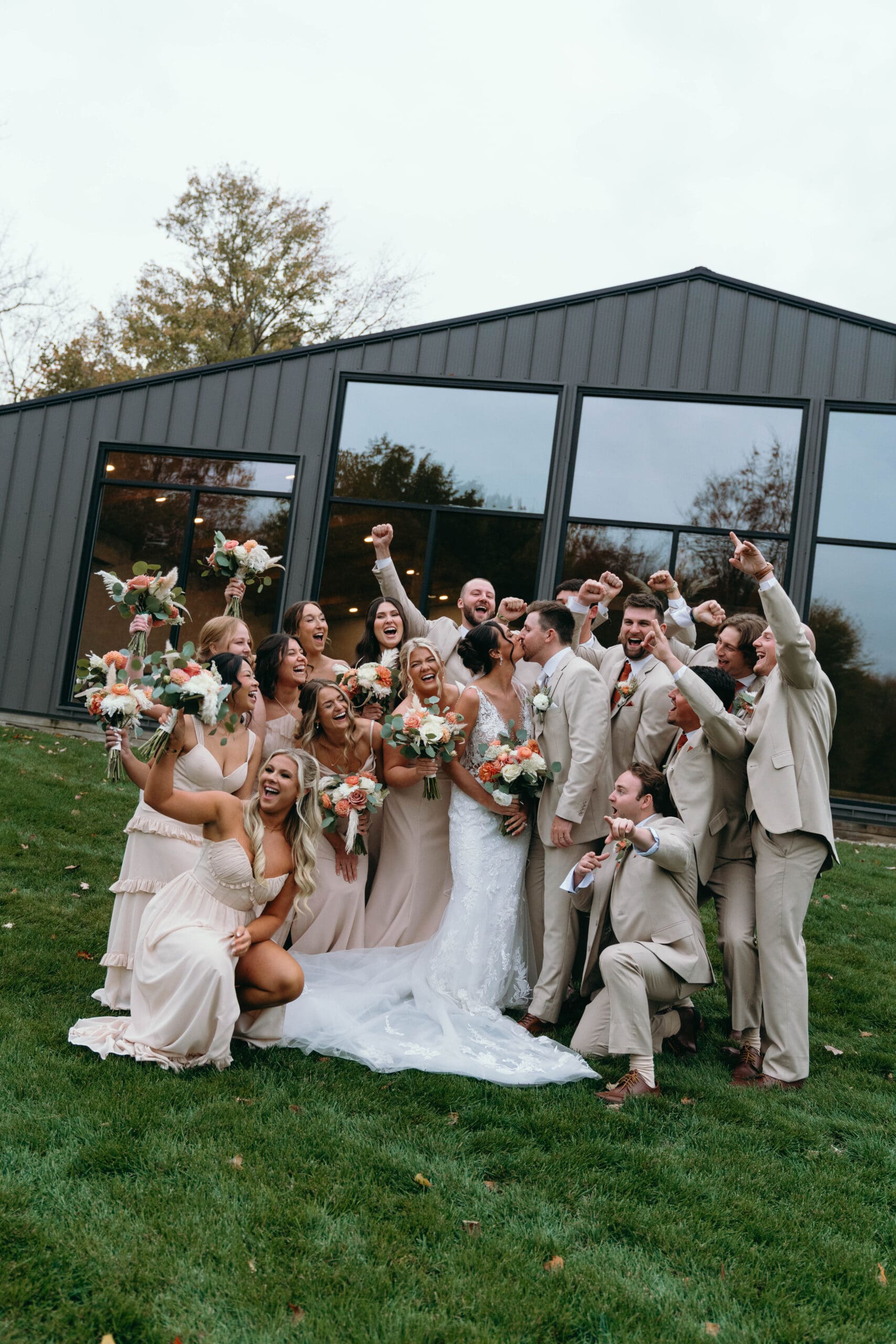 a large wedding party being photographed by Cassandra lee photo at standing rock farm in Madison ohio cheering as the bride and groom kiss