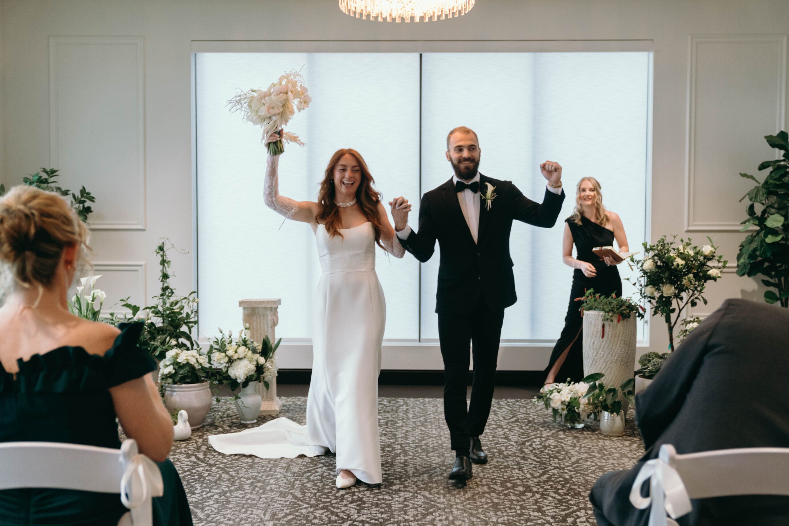 A bride and groom bring photographed by Cassandra Lee Photo walking up the aisle at the Legacy Hotel in Green Bay, Wisconsin, cheering after they just said, "I do."